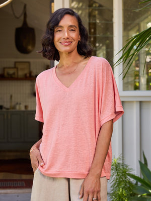 Woman wearing a pink shirt standing in a home setting with plants.