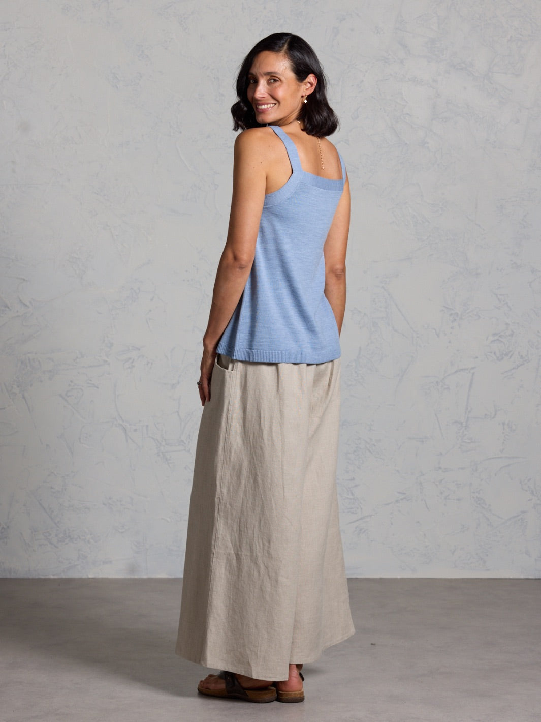 Woman wearing a light blue sleeveless top and beige skirt against a gray background