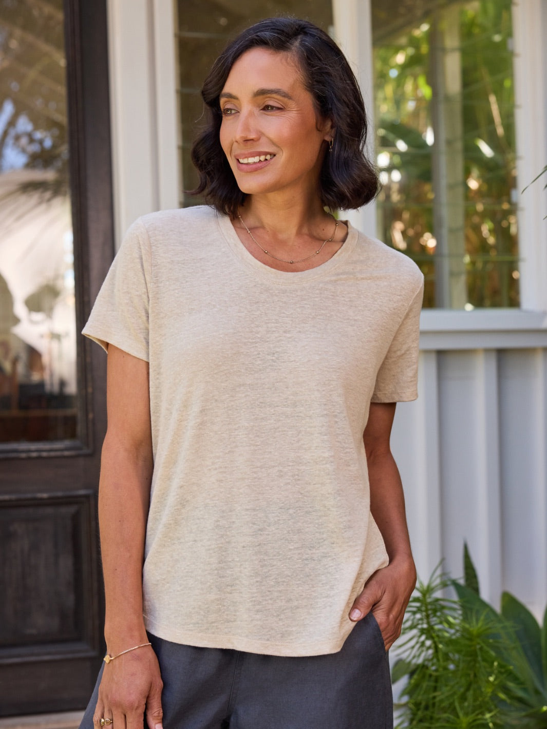 Woman wearing a beige t-shirt and dark pants standing outdoors.