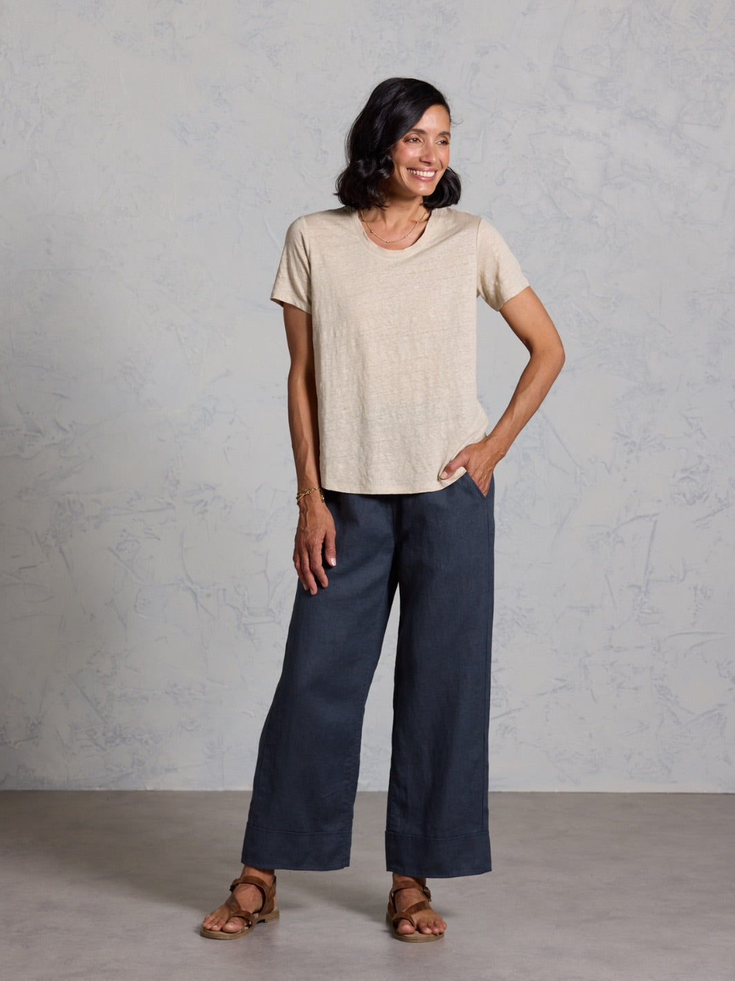 Woman wearing a beige top and black pants against a gray background