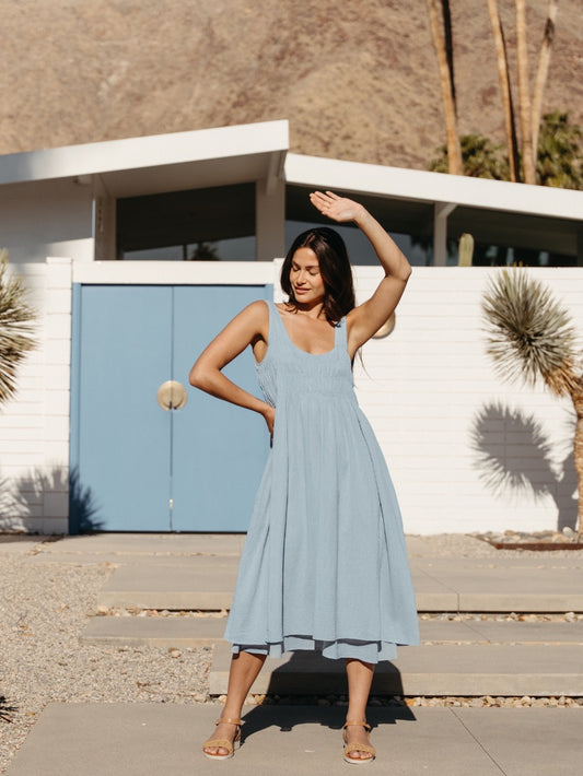 Woman in a light blue dress standing in front of a modern house with palm trees.