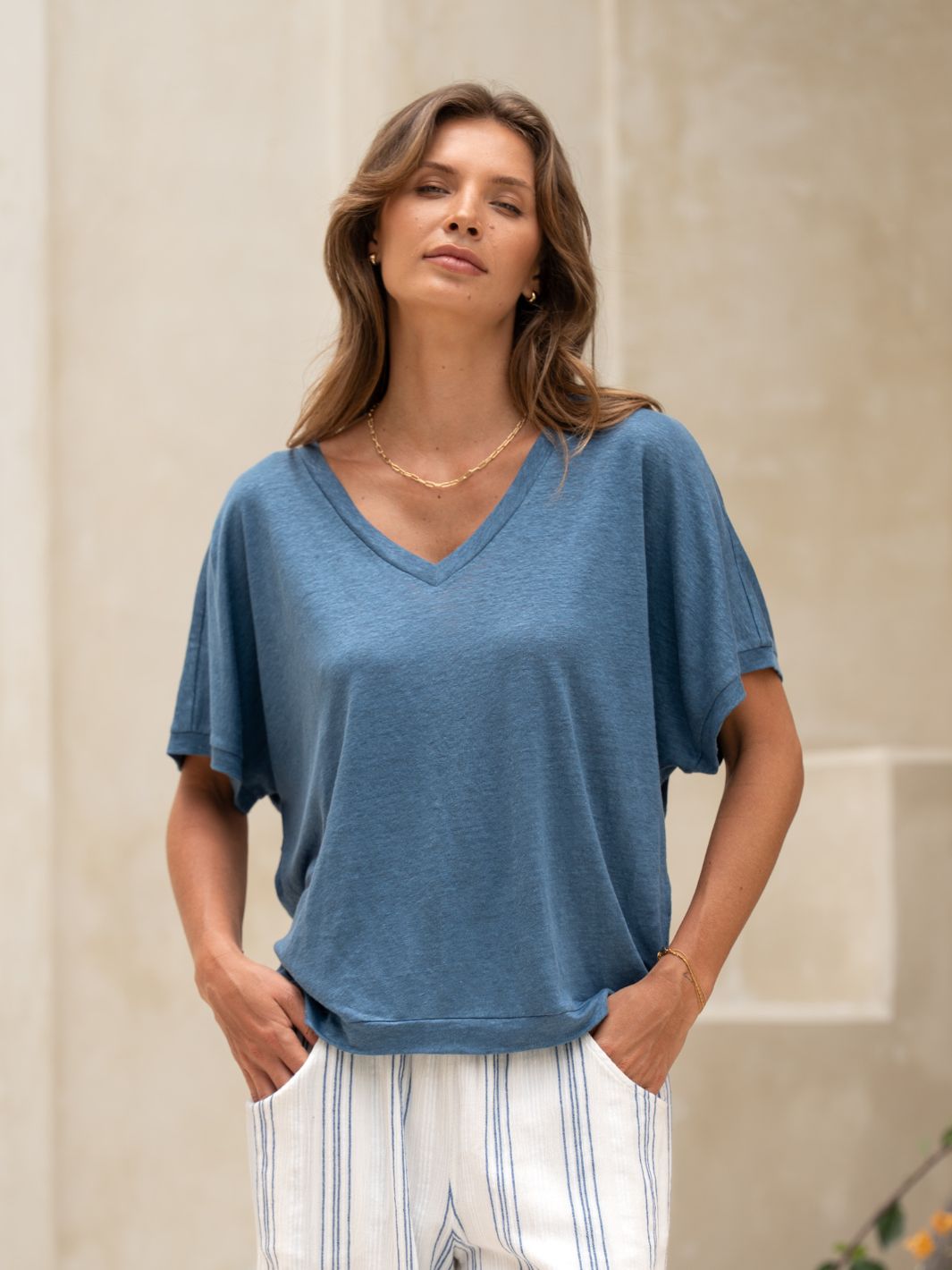 Woman wearing a blue top and stripe pants on a neutral background.