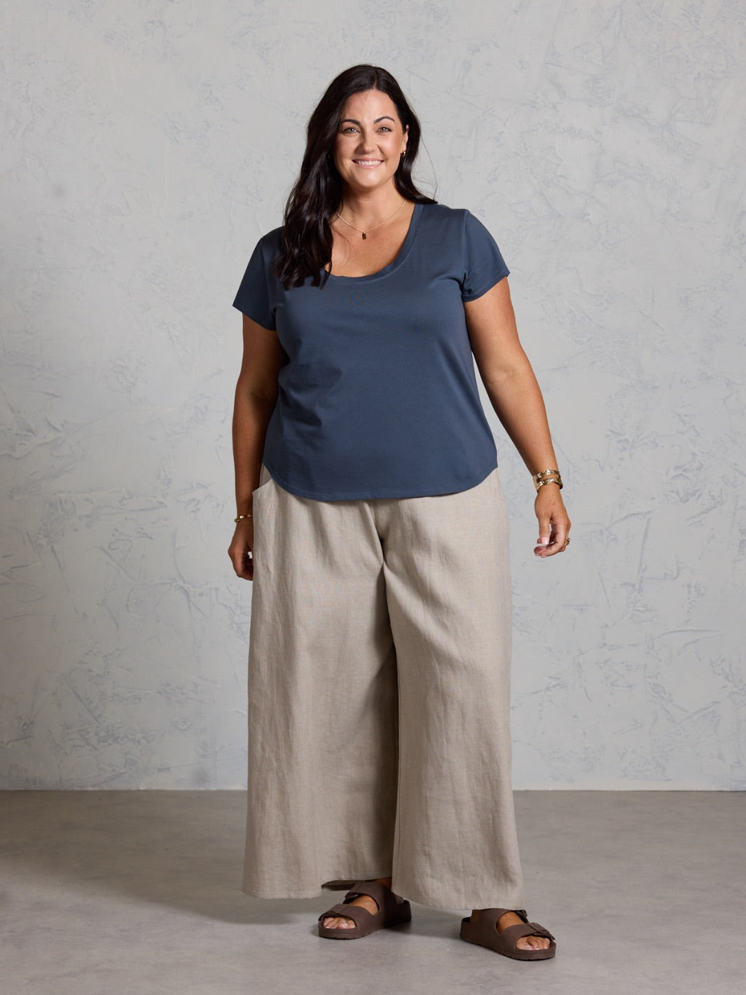 Woman wearing a black top and beige pants against a plain background