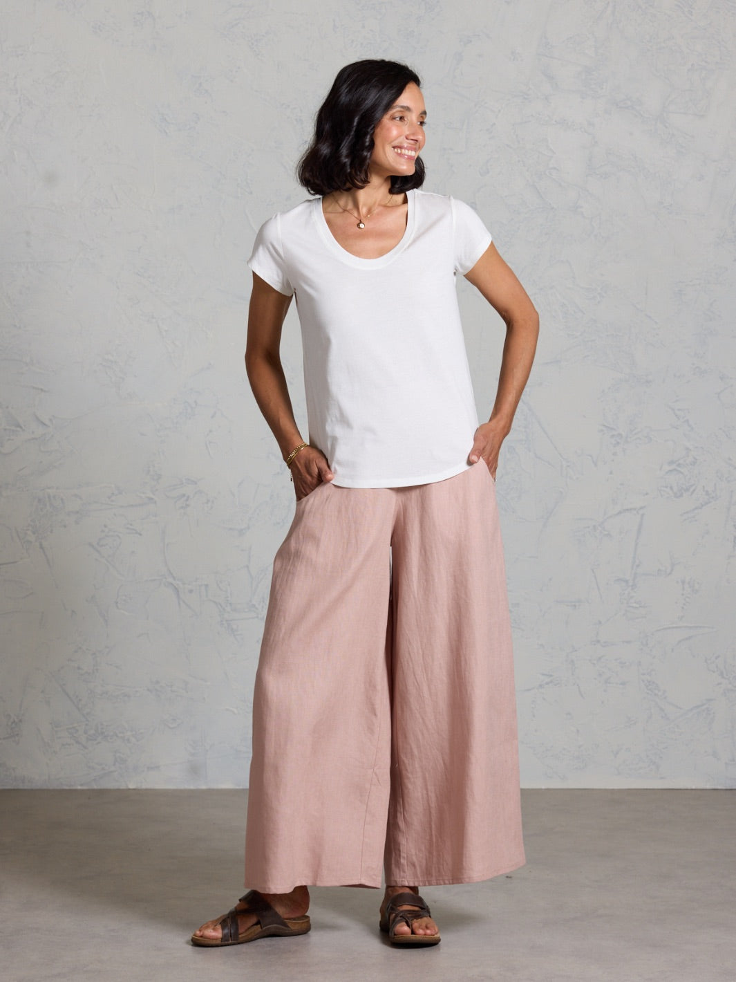 Woman wearing a white t-shirt and pink wide-leg pants against a gray background