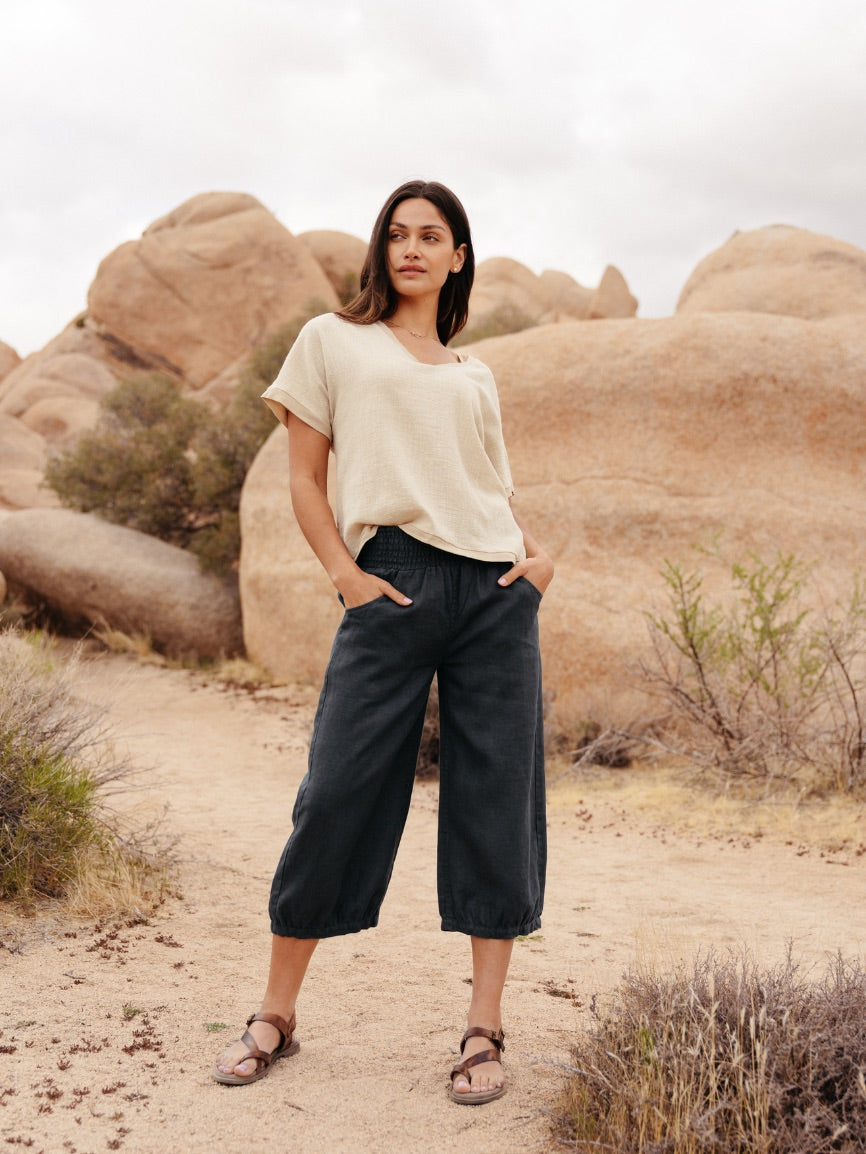 Woman standing in a desert landscape with rocky formations and sparse vegetation.