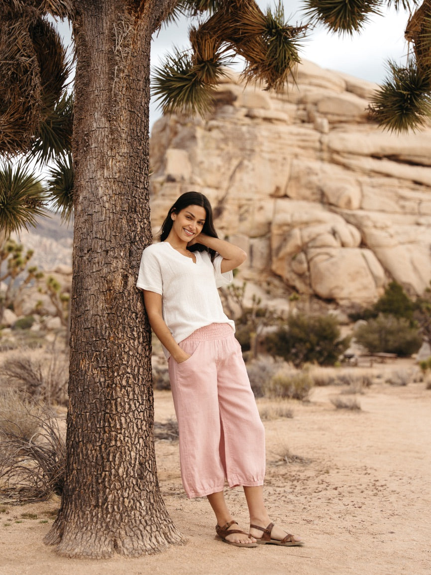 Woman leaning against a tree in a desert landscape with rocky formations.