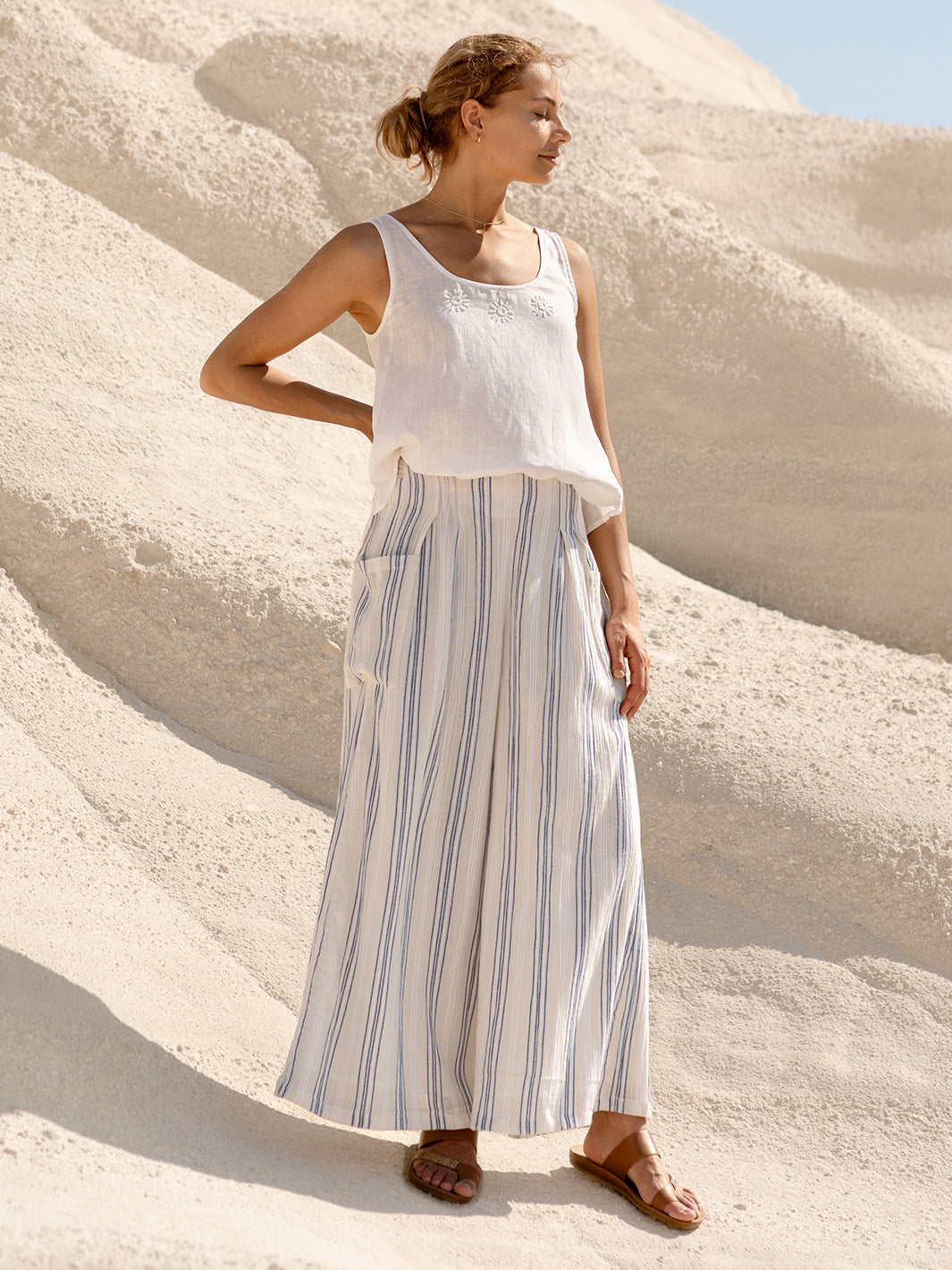 Woman in a white top and striped pants standing on sand dunes