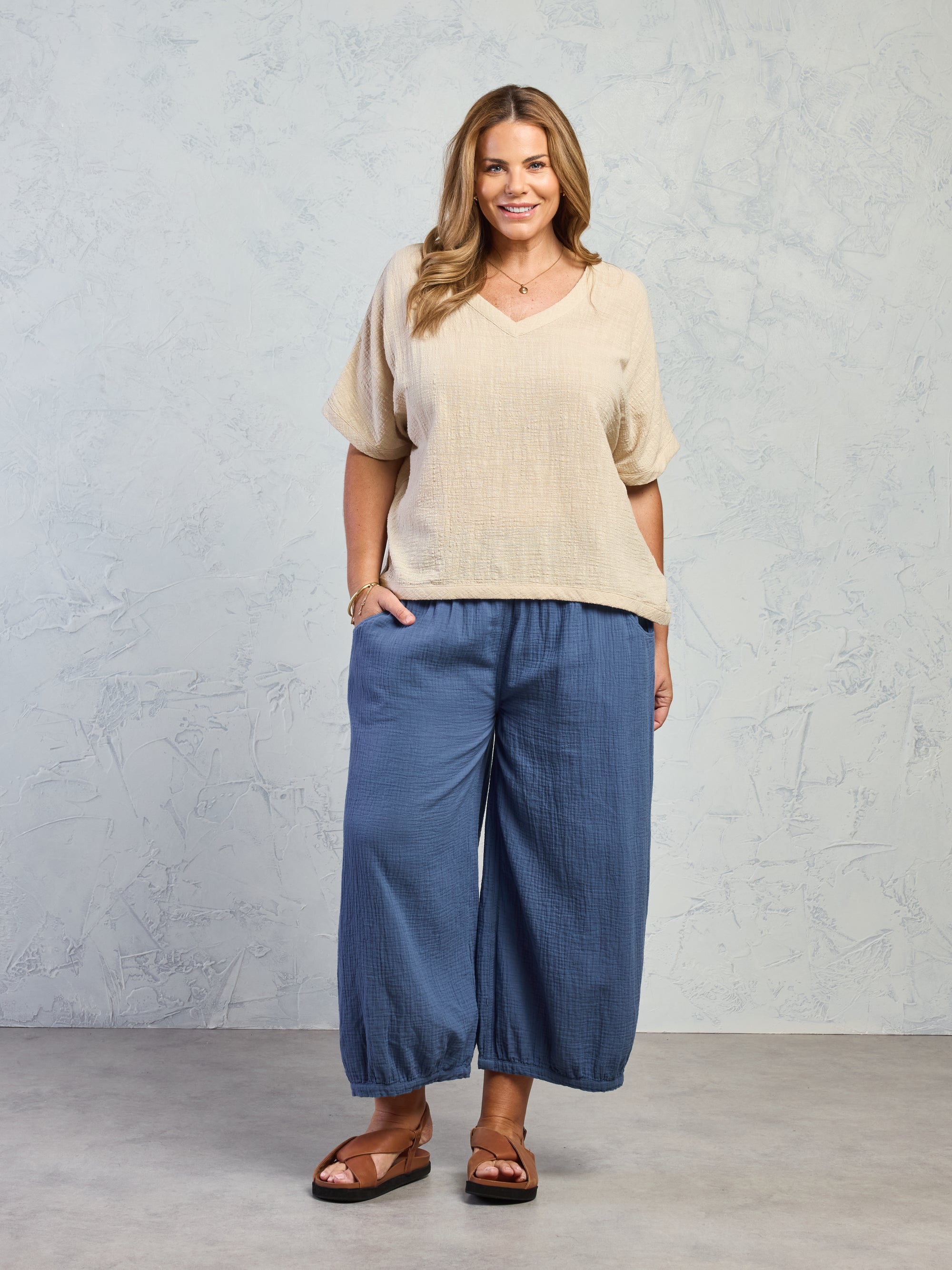 Woman wearing a beige top and blue pants against a gray background