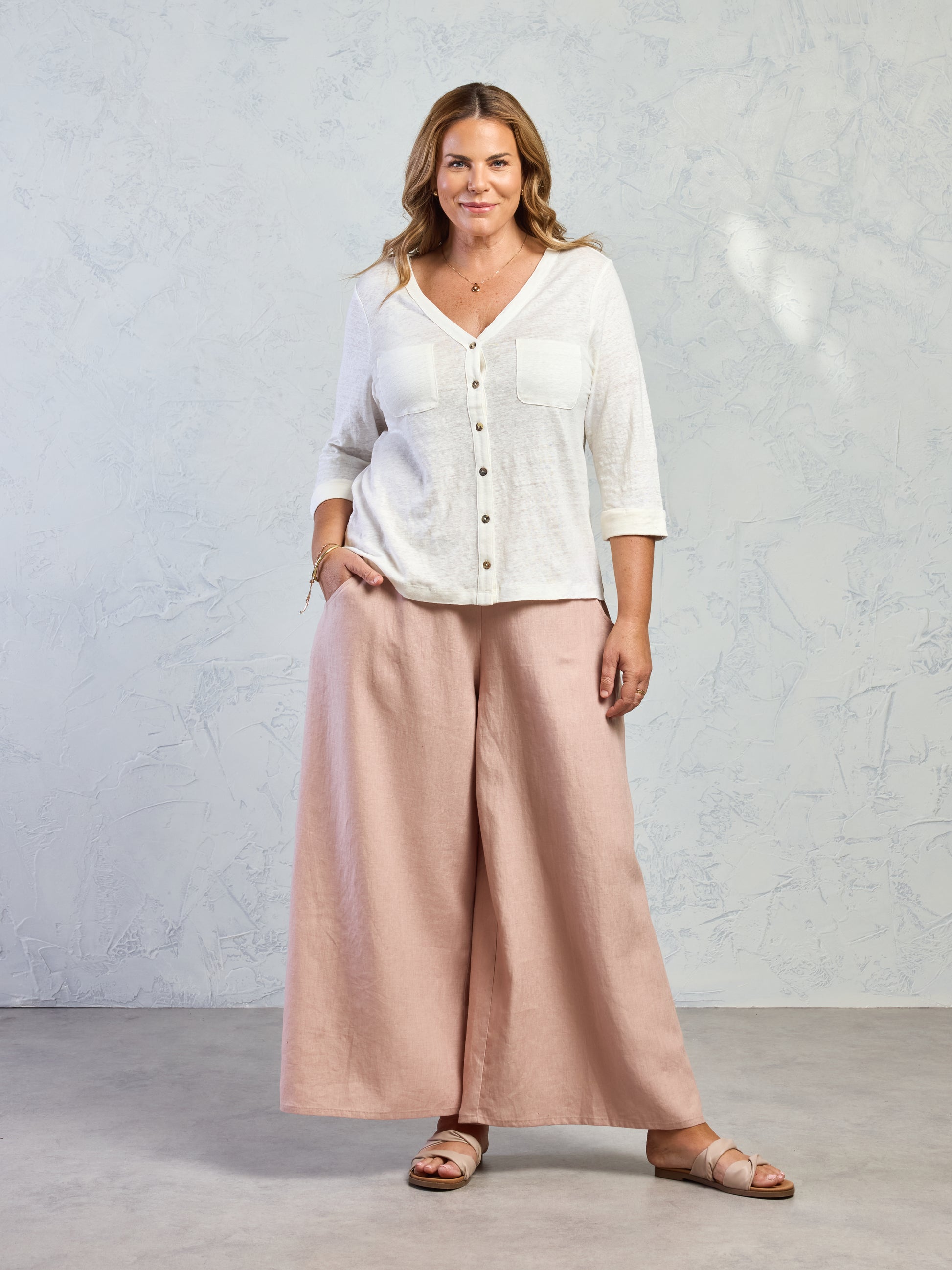 Woman wearing a white blouse and beige wide-leg pants against a plain background