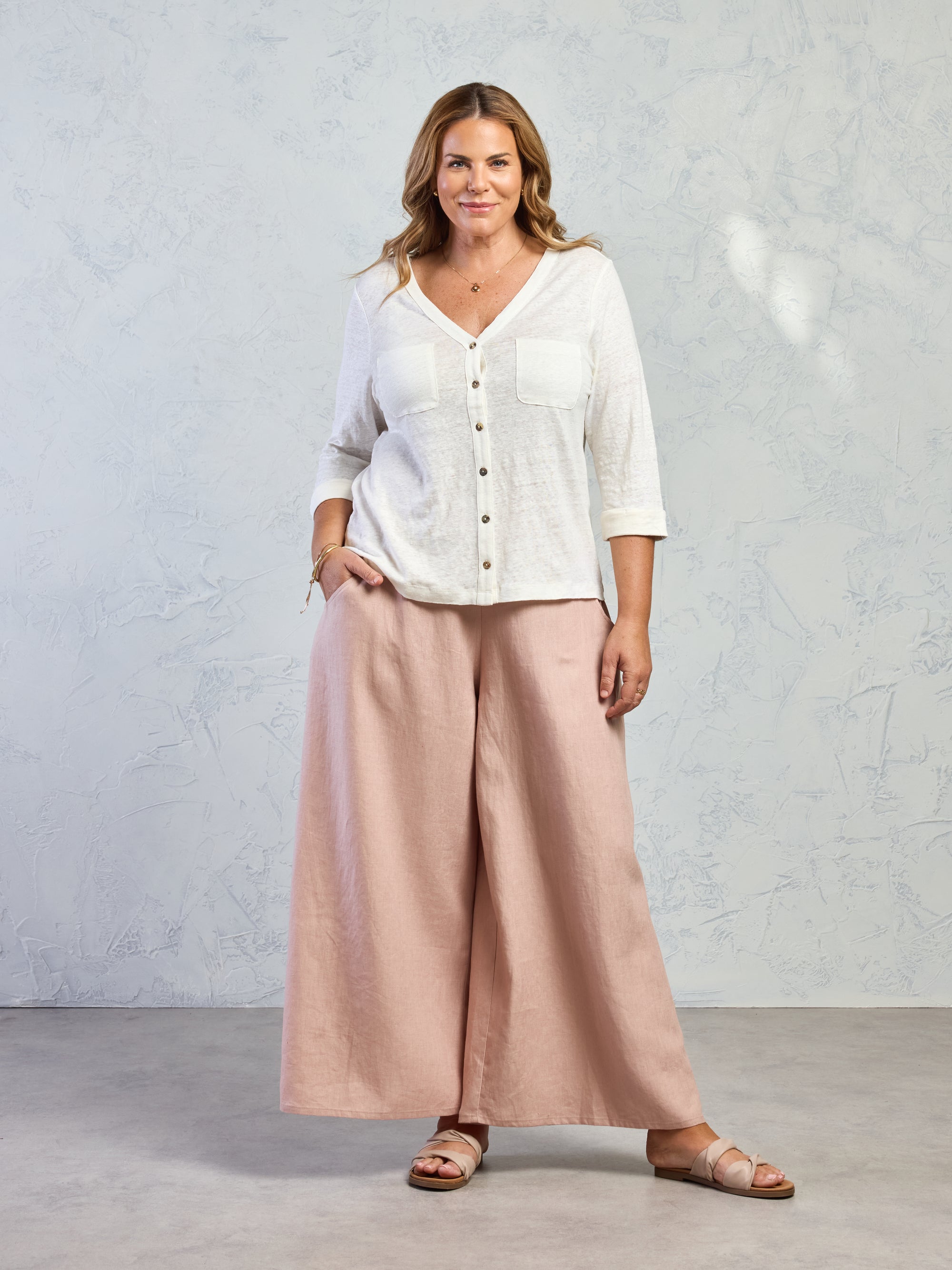 Woman wearing a white blouse and beige wide-leg pants against a plain background
