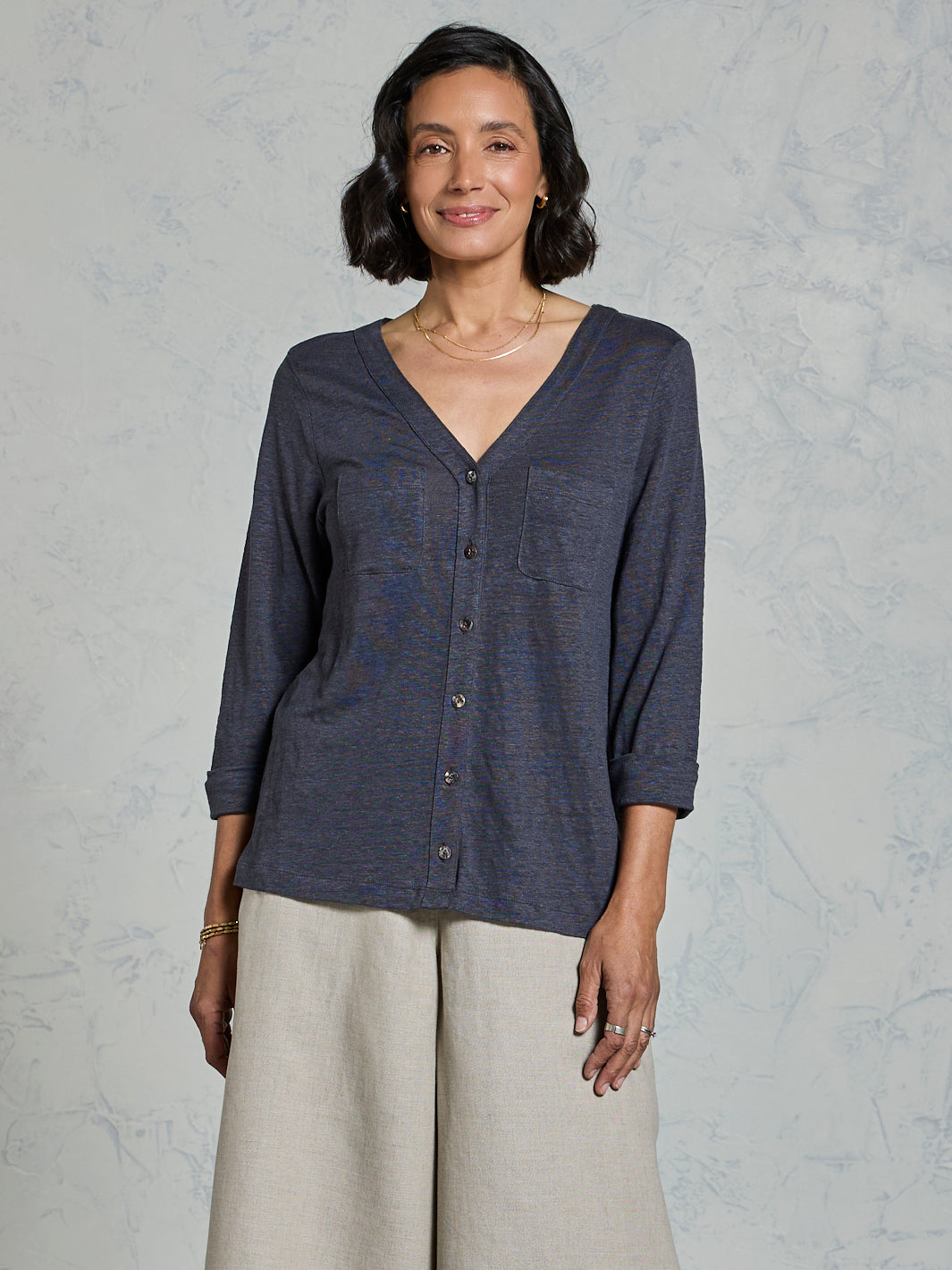 Woman wearing a dark blue button-up shirt and light gray pants against a plain background