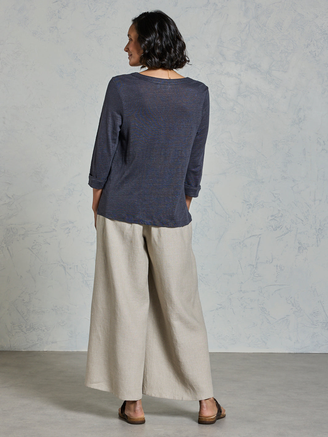 Woman wearing a dark blue top and beige pants against a gray background