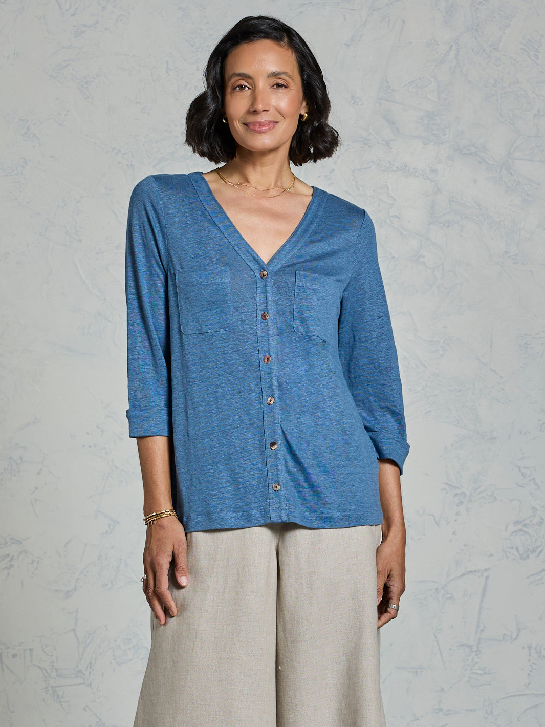 Woman wearing a blue button-up shirt and beige pants against a gray background