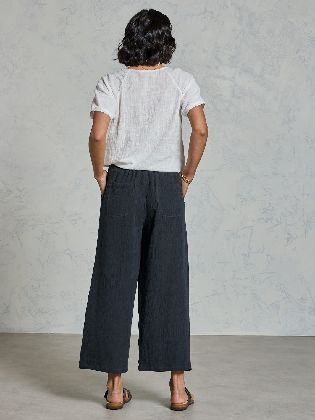 Person wearing a white shirt and dark pants against a gray background