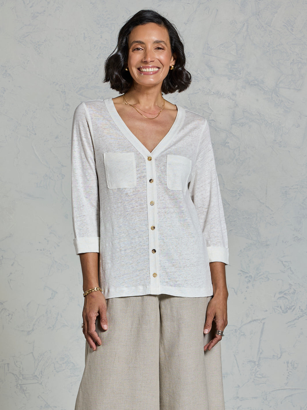 Woman wearing a white button-up shirt and beige pants against a gray background