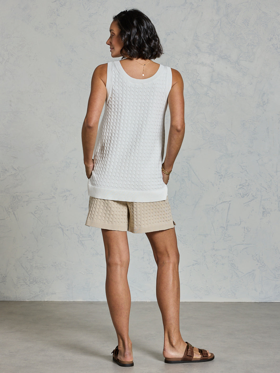 Woman wearing a white sleeveless top and beige shorts against a gray background