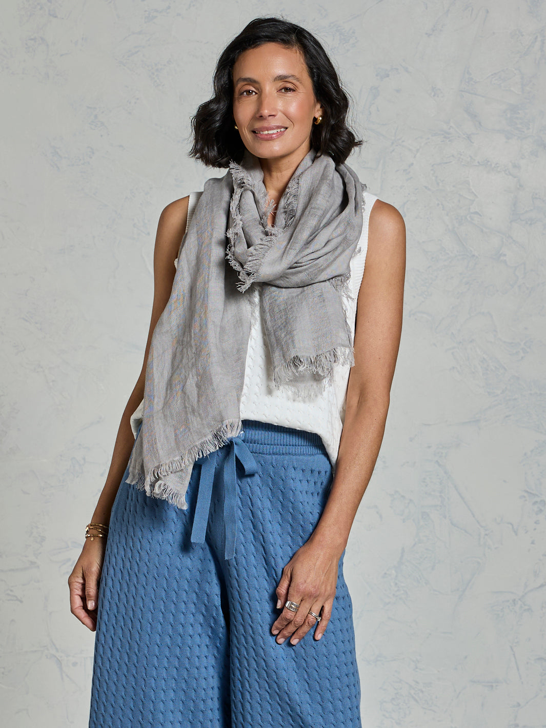 Woman wearing a gray scarf and blue pants against a plain background
