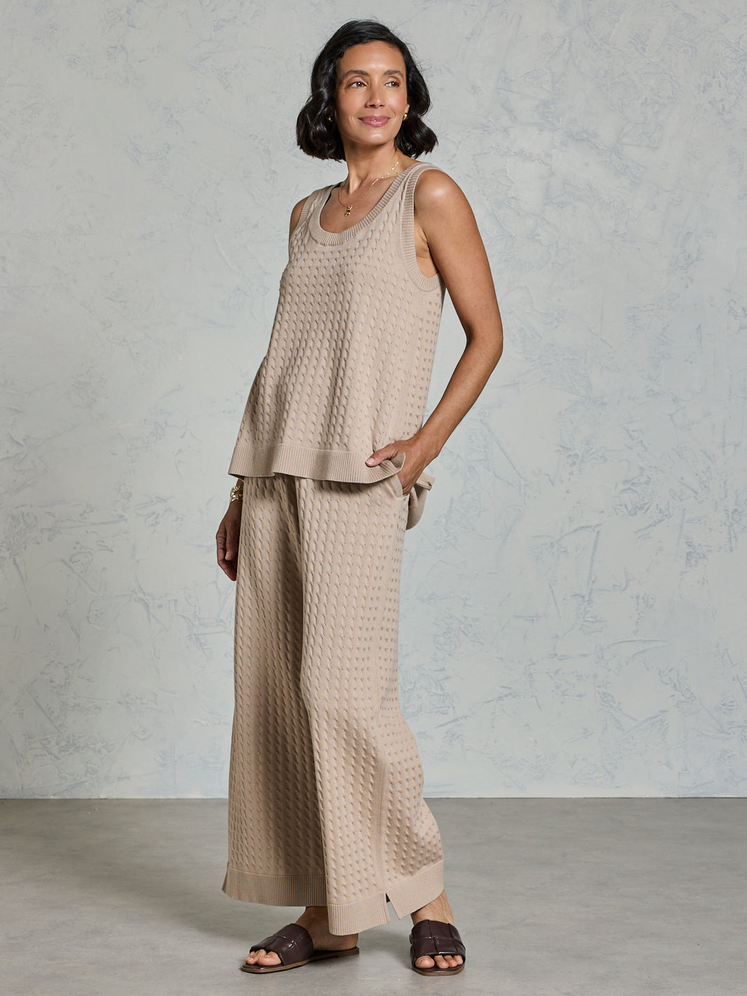 Woman wearing a beige sleeveless top and wide-leg pants against a plain background