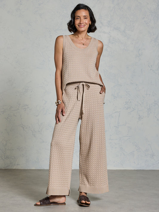 Woman wearing a beige sleeveless top and wide-leg pants against a plain background