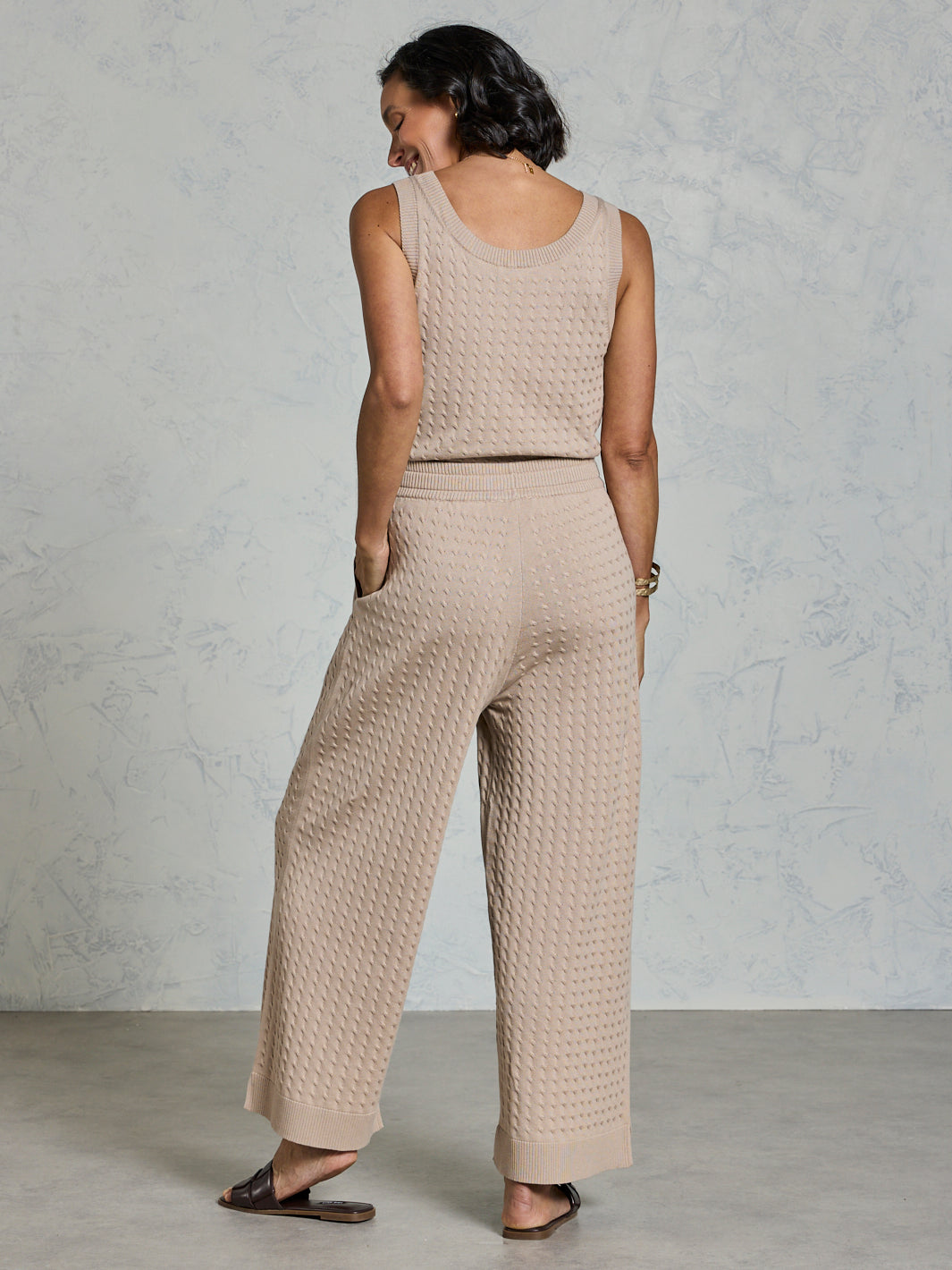 Woman wearing a beige textured sleeveless top and wide-leg pants against a plain background
