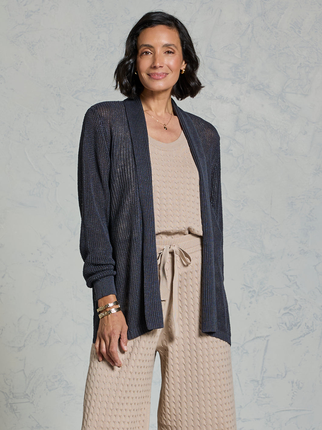 Woman wearing a navy cardigan over a beige top and pants on a light gray background