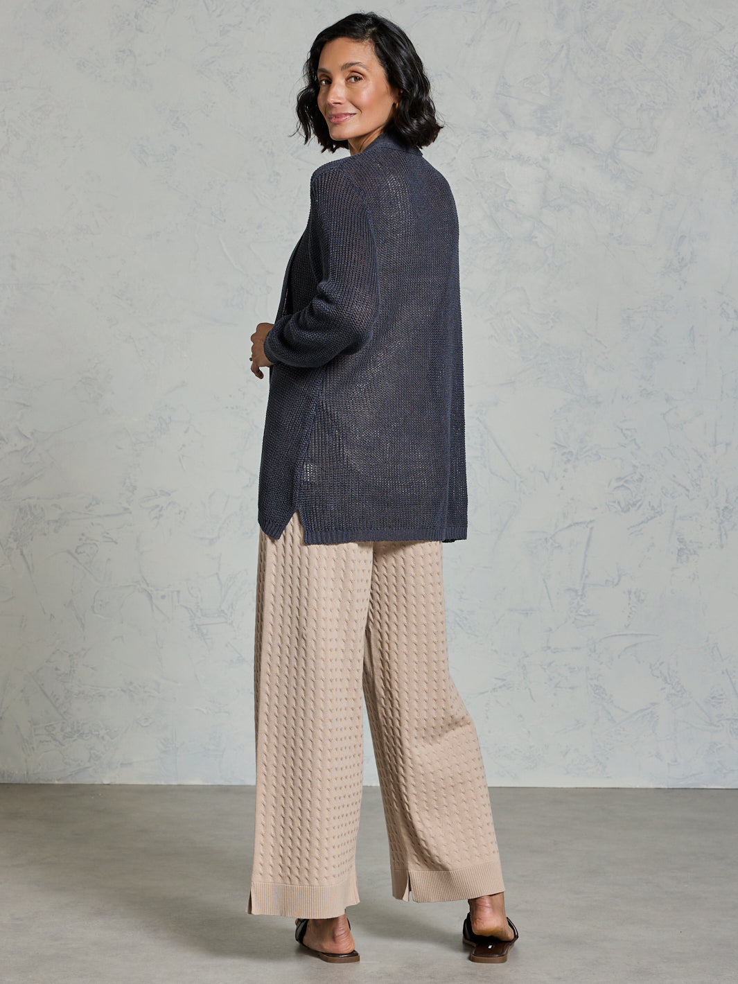 Woman wearing a dark blue textured jacket and beige pants against a gray background