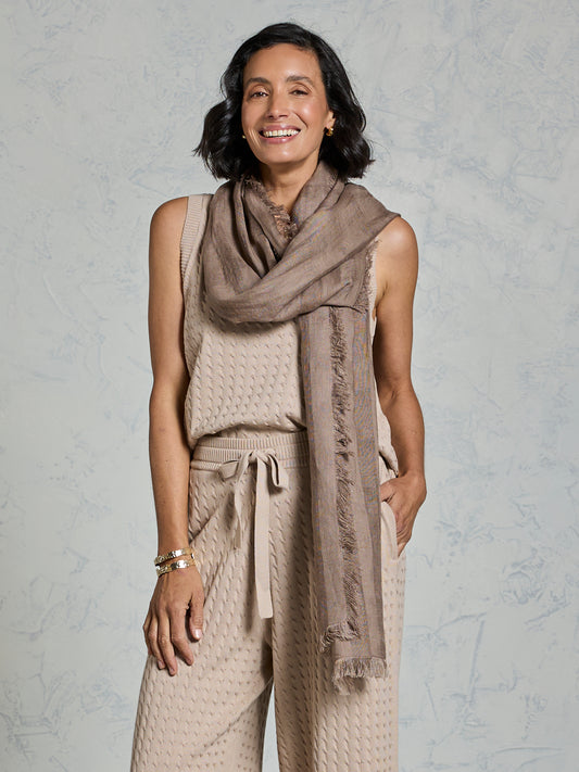 Woman wearing a beige sleeveless top and pants with a matching scarf against a gray background