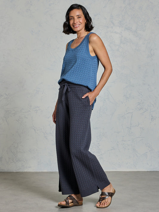 Woman wearing a blue sleeveless top and dark pants against a gray background