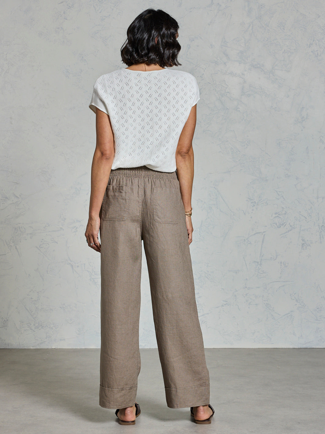 Person wearing a white top and brown wide-leg pants against a plain background