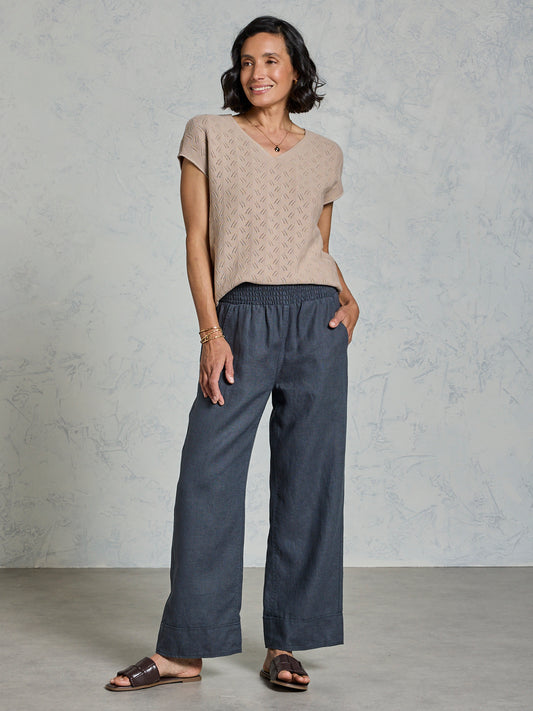 Woman wearing a beige patterned top and dark blue pants against a gray background