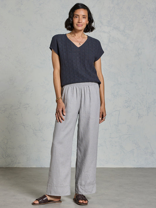 Woman wearing a dark blue top and light gray pants against a plain background
