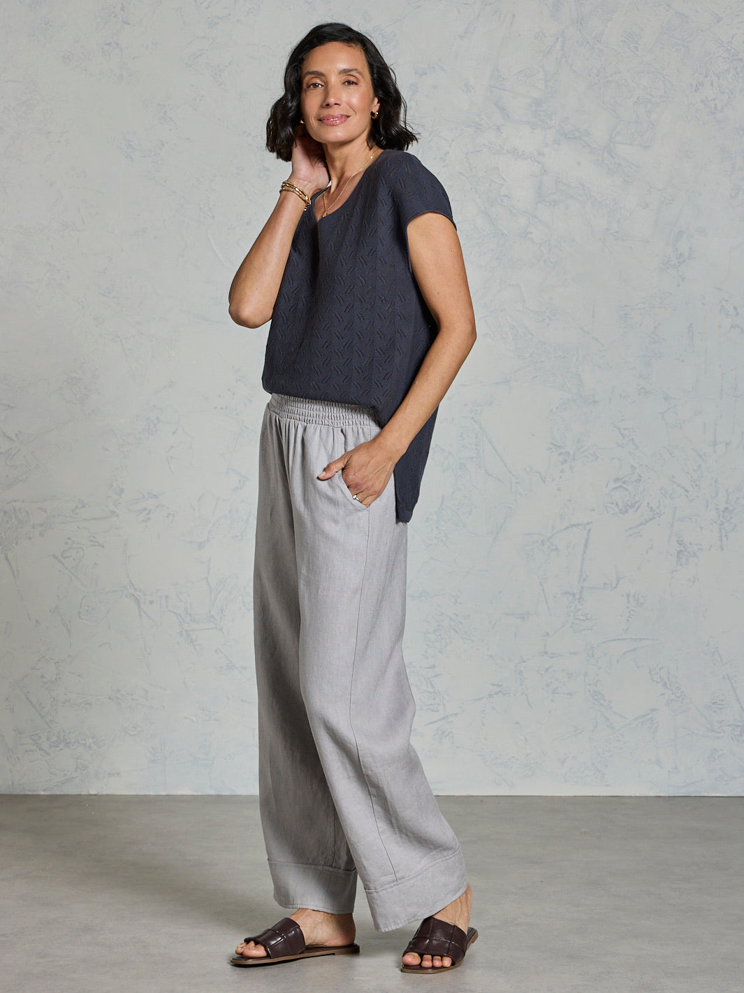 Woman wearing a dark blue top and light gray pants against a plain background