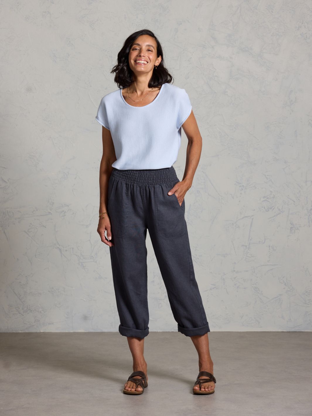 Woman wearing a white t-shirt and dark pants against a plain background
