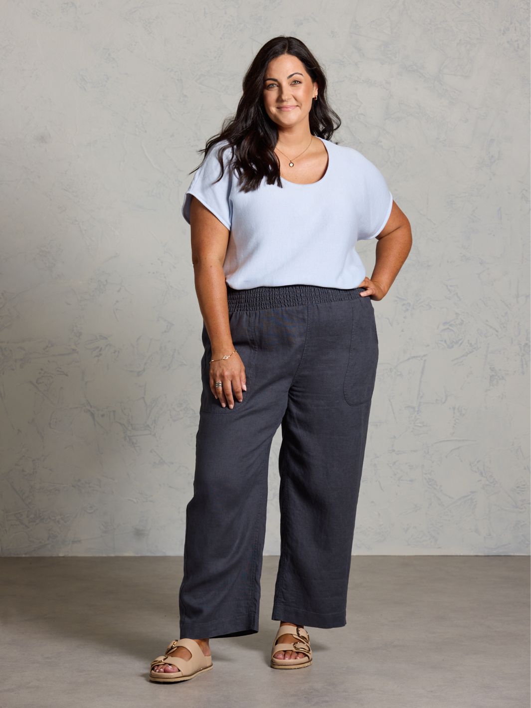 Woman wearing a light blue top and dark gray pants against a plain background