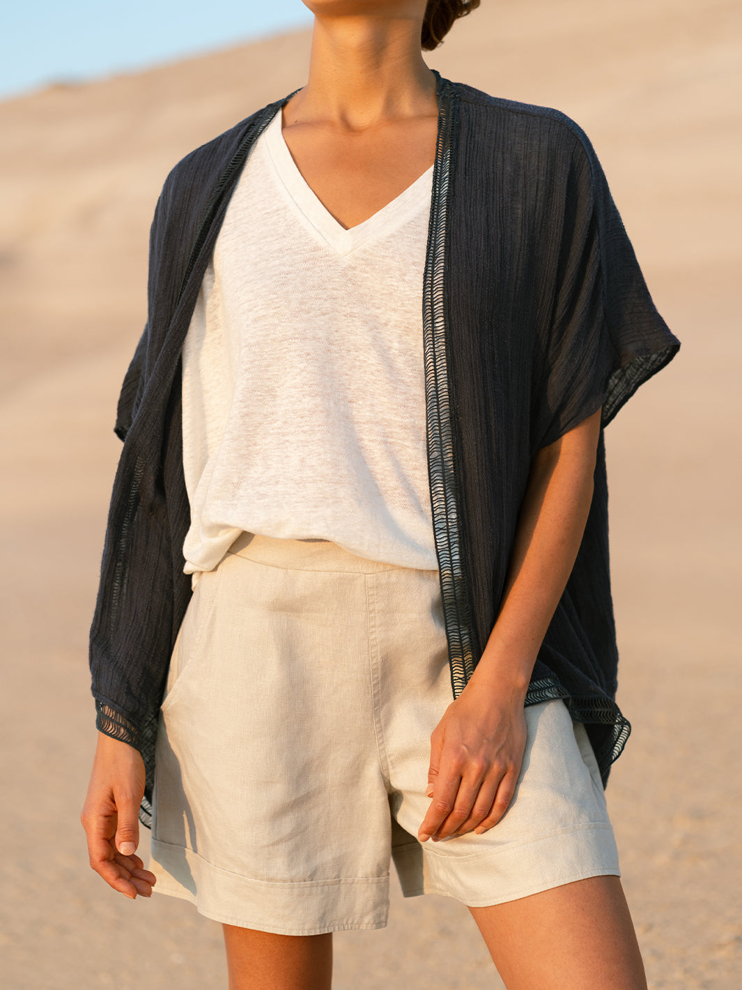Person wearing a black cardigan, white shirt, and beige shorts against a desert background