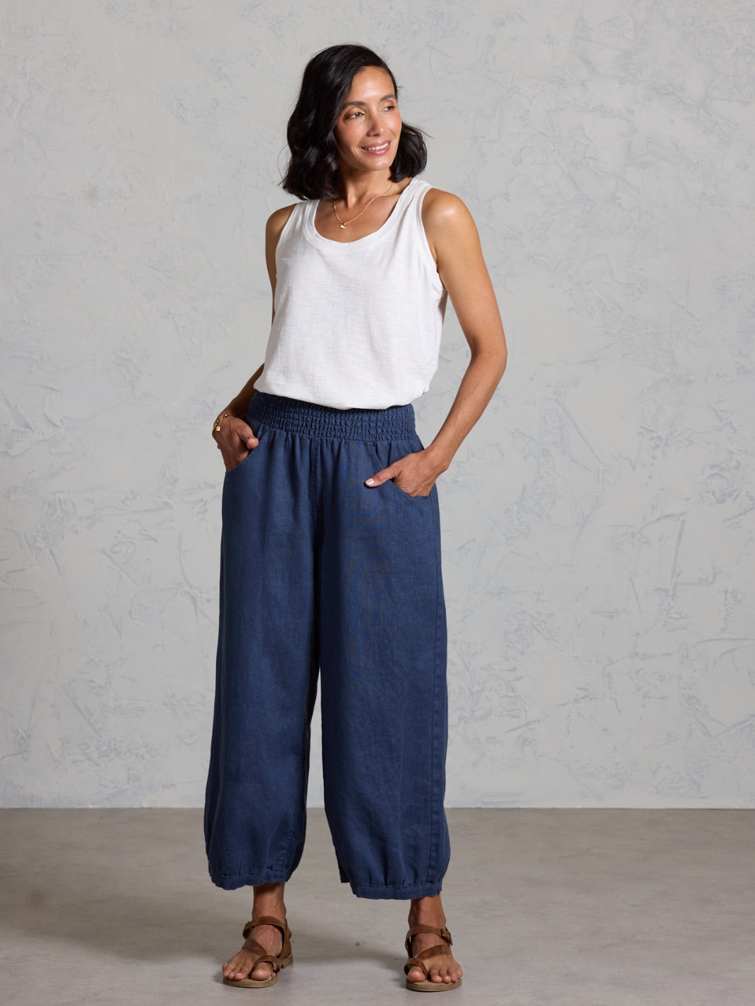 Woman wearing a white sleeveless top and blue wide-leg pants against a gray background