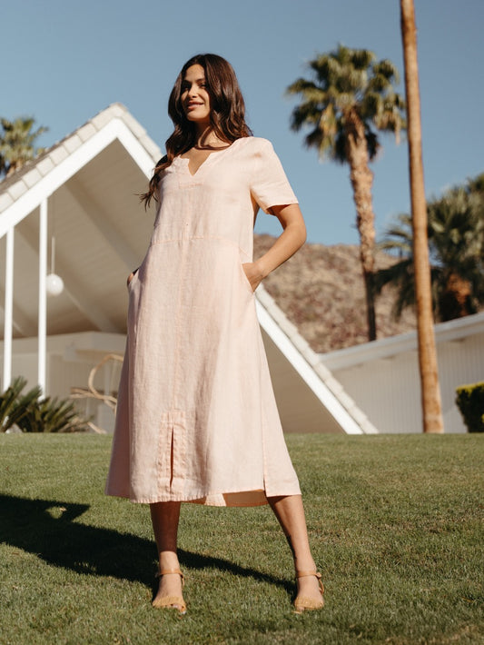 Woman in a light pink dress standing on grass with palm trees in the background