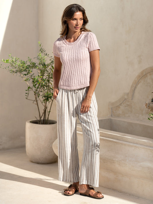 Model wearing the Agni Cotton Linen Knit Top in rosewater with striped linen drawstring pants in a sunlit stone courtyard.