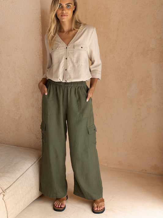 A model wearing olive green cargo pants with a relaxed fit and side pockets, paired with a beige button-up shirt.