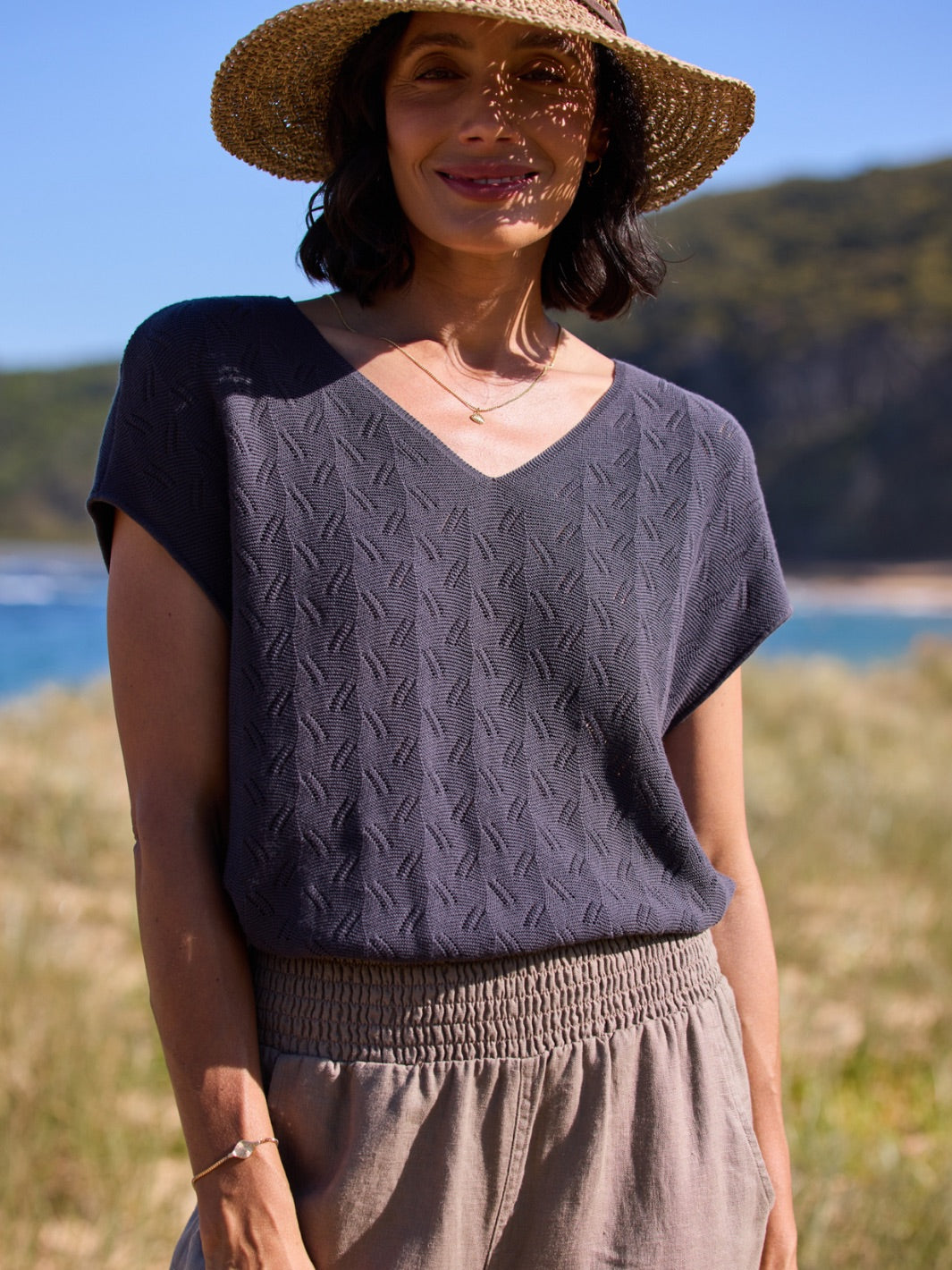 Woman wearing a dark knitted top and beige hat outdoors with a scenic background