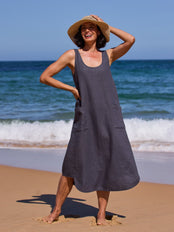 Woman in a dark dress and straw hat standing on a beach with ocean waves in the background