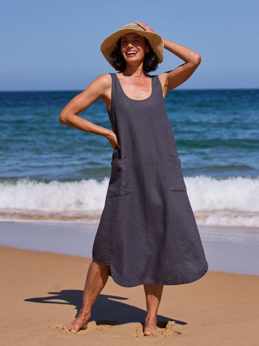 Woman in a dark dress and straw hat standing on a beach with ocean waves in the background