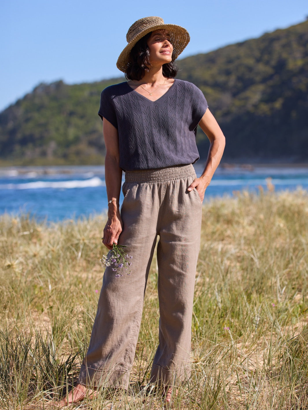 Woman standing in a grassy field with mountains and water in the background