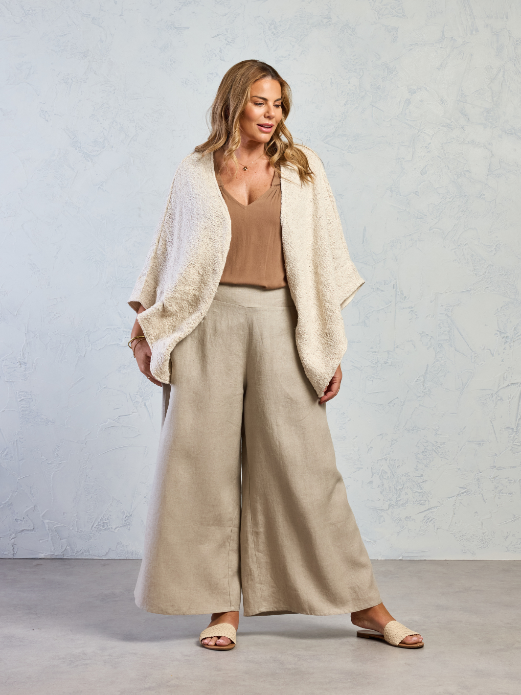 Woman wearing a beige cardigan, brown top, and wide-leg pants against a light gray background