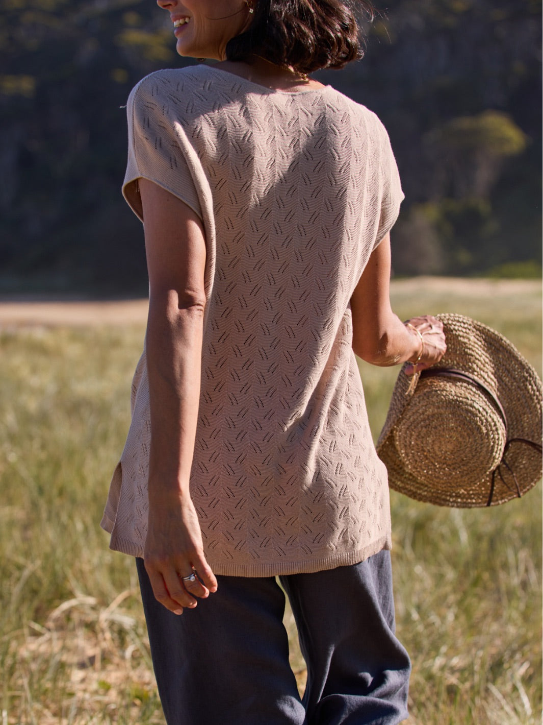 Woman wearing a beige patterned shirt and holding a straw hat in a field