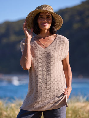 Woman wearing a beige cable knit top and straw hat by a body of water.