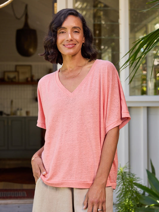 Woman wearing a pink shirt standing in a home setting with plants.