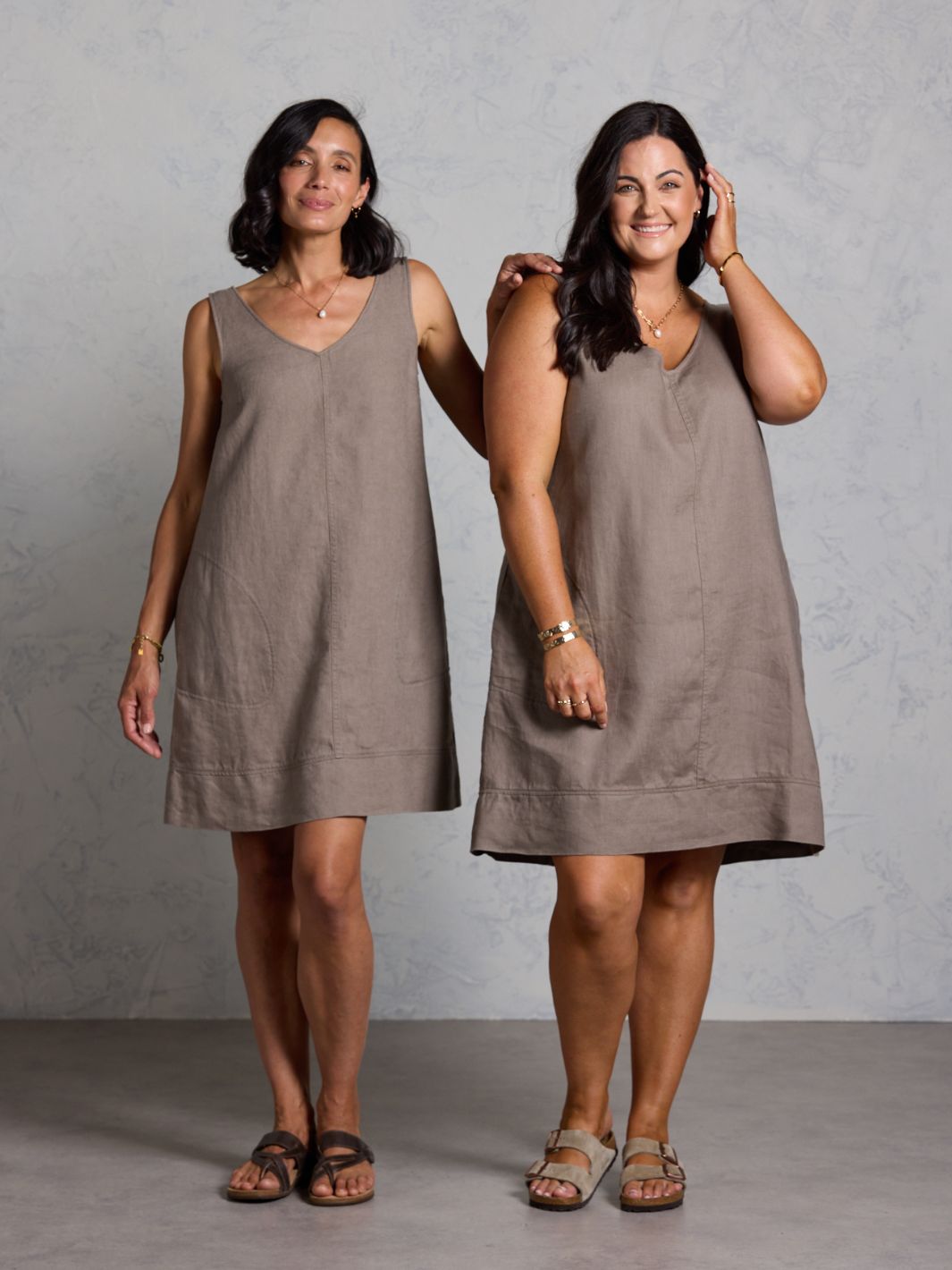 Two women wearing brown sleeveless dresses against a plain background