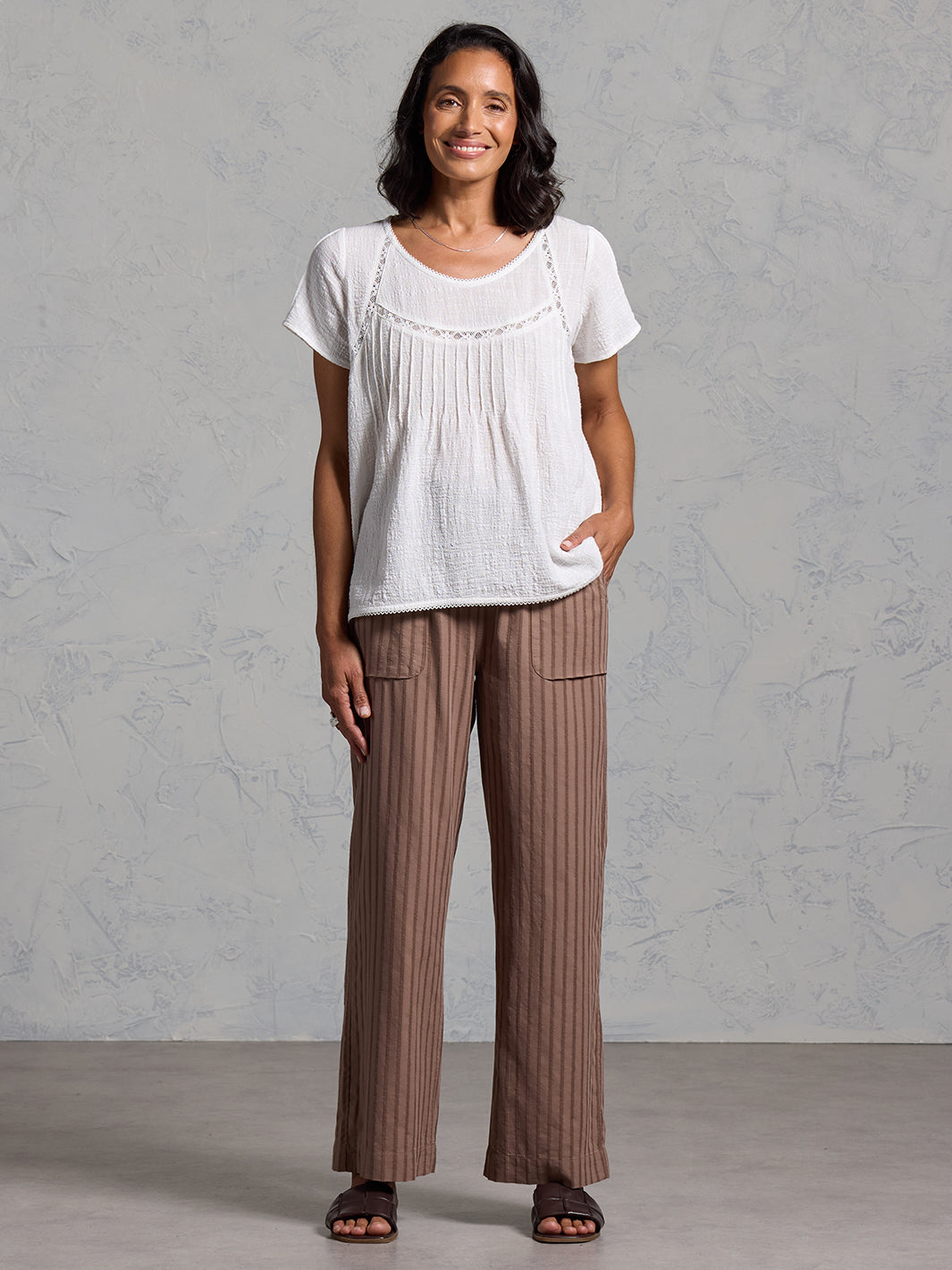 Woman wearing a white top and brown striped pants against a gray background