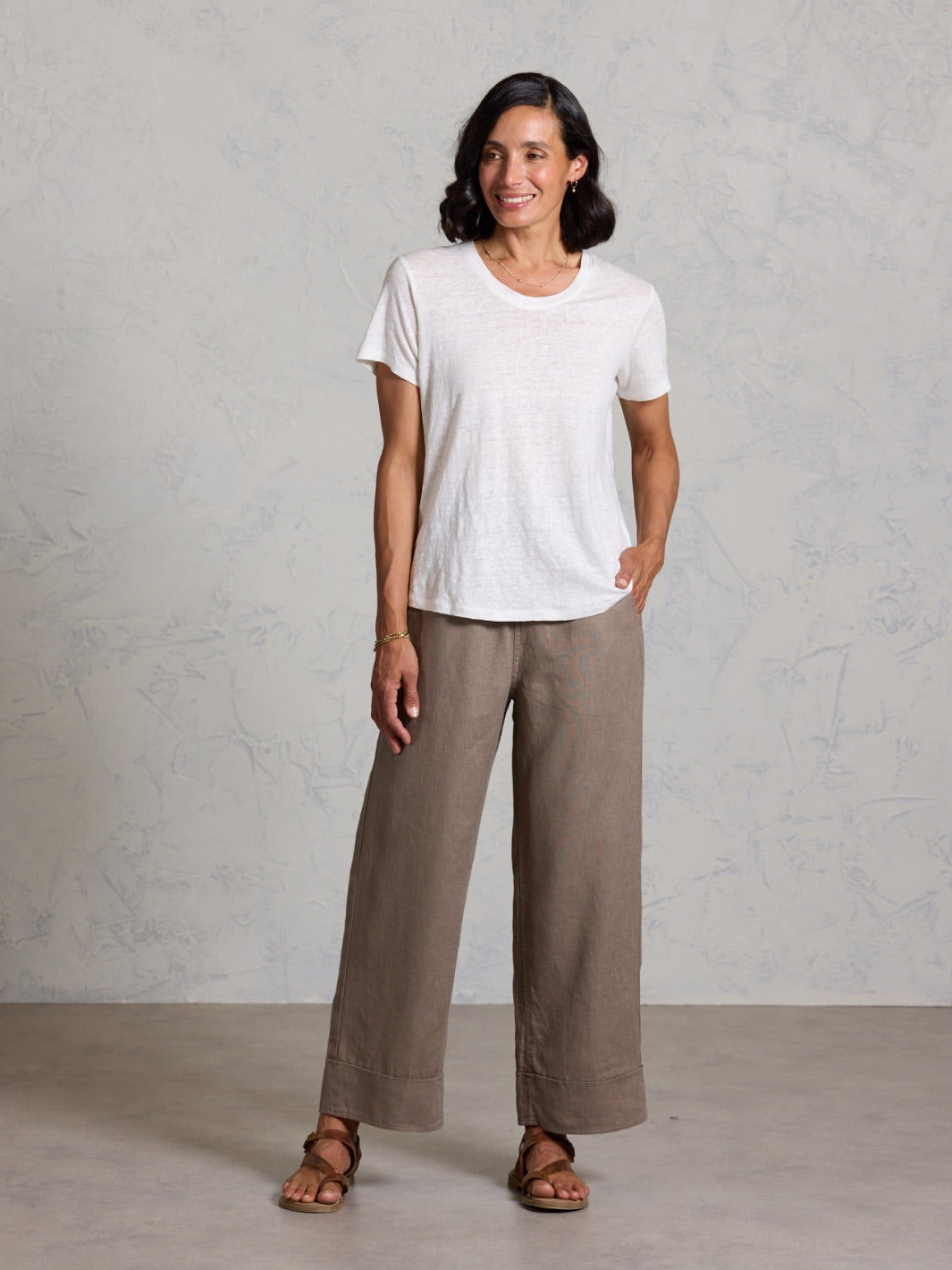 Woman wearing a white t-shirt and brown pants against a gray background